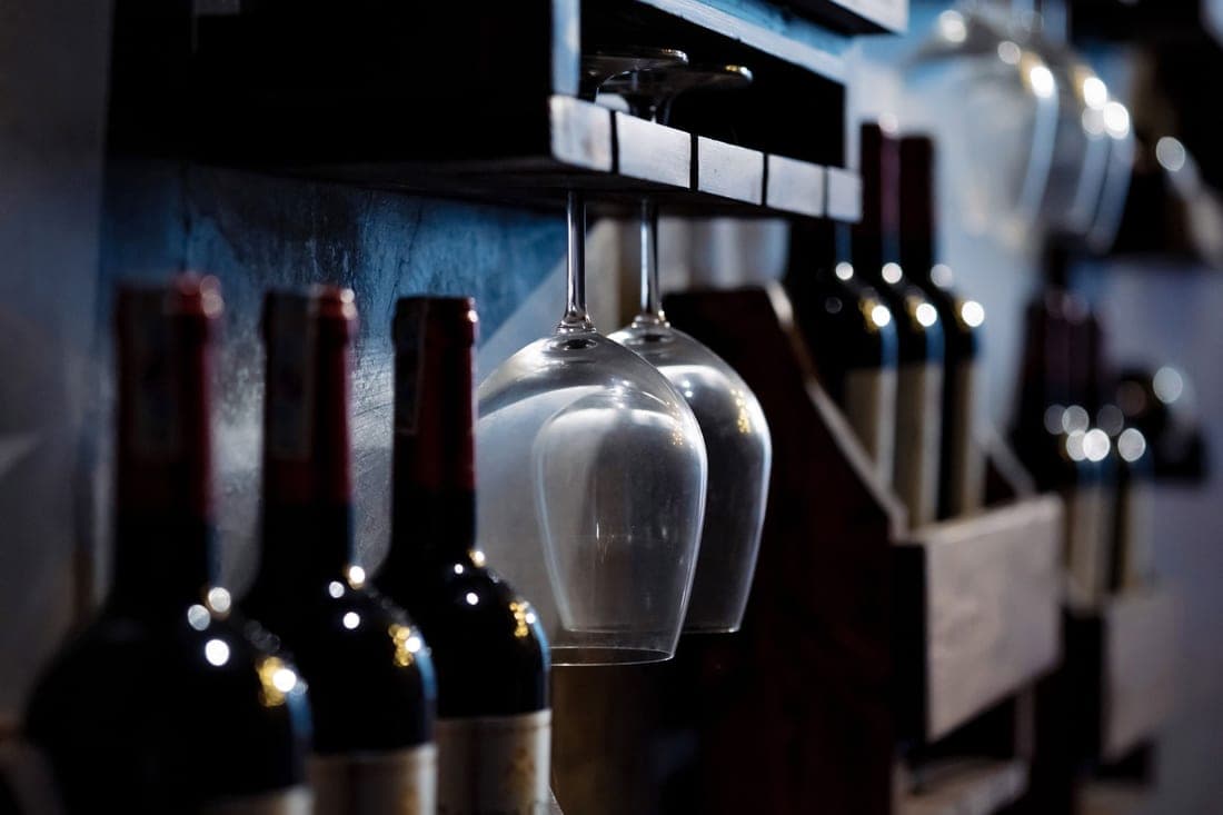 A wooden bar cabinet with glass doors and bottles inside