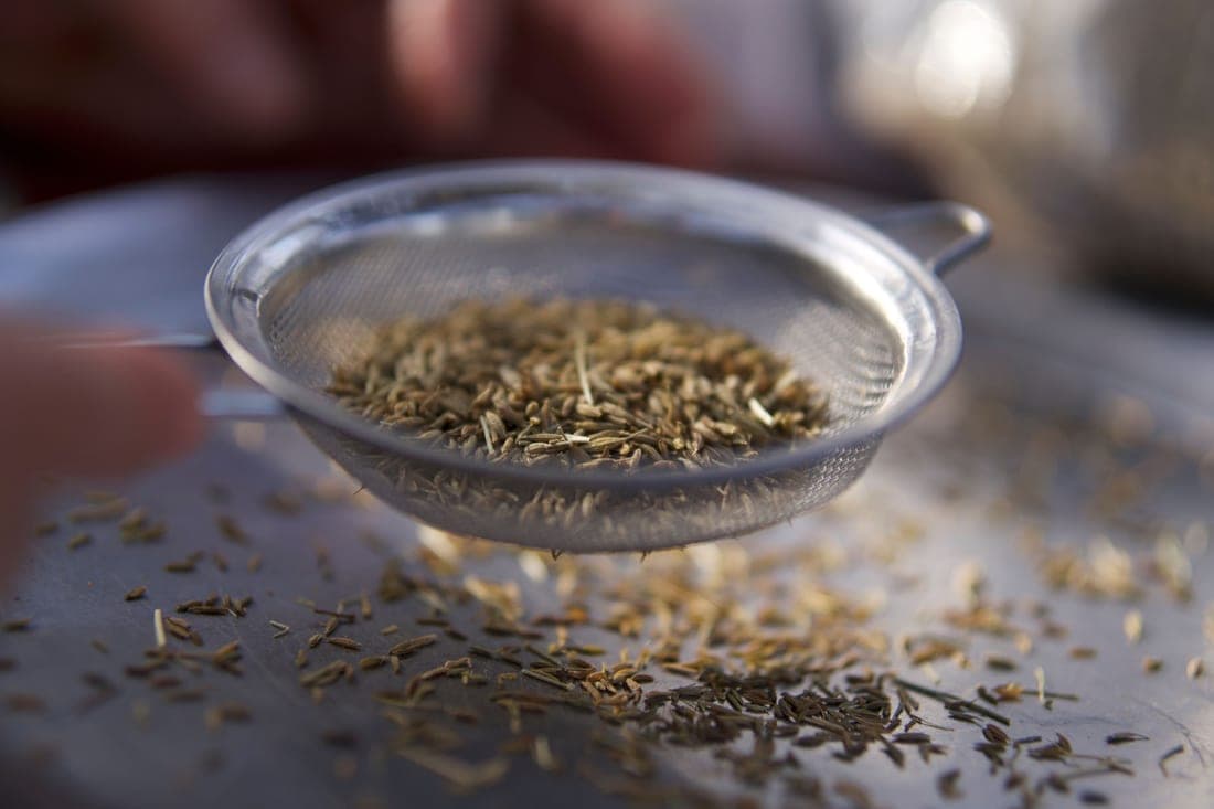 Herbs being strained through a fine conical mesh sieve