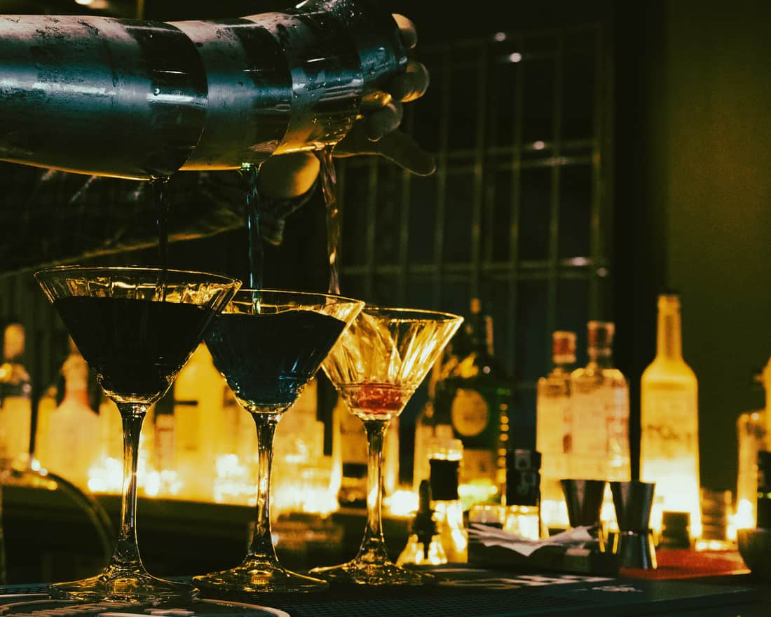 A bartender straining a cocktail into a glass on a dark bar