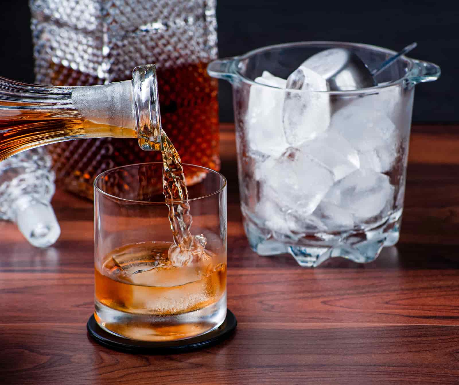 Whiskey being poured over a clear ice sphere