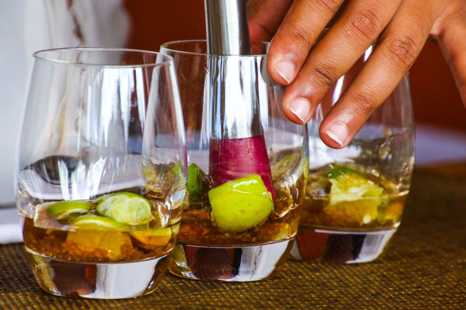 Three rocks glasses of muddled fruit beside a muddler