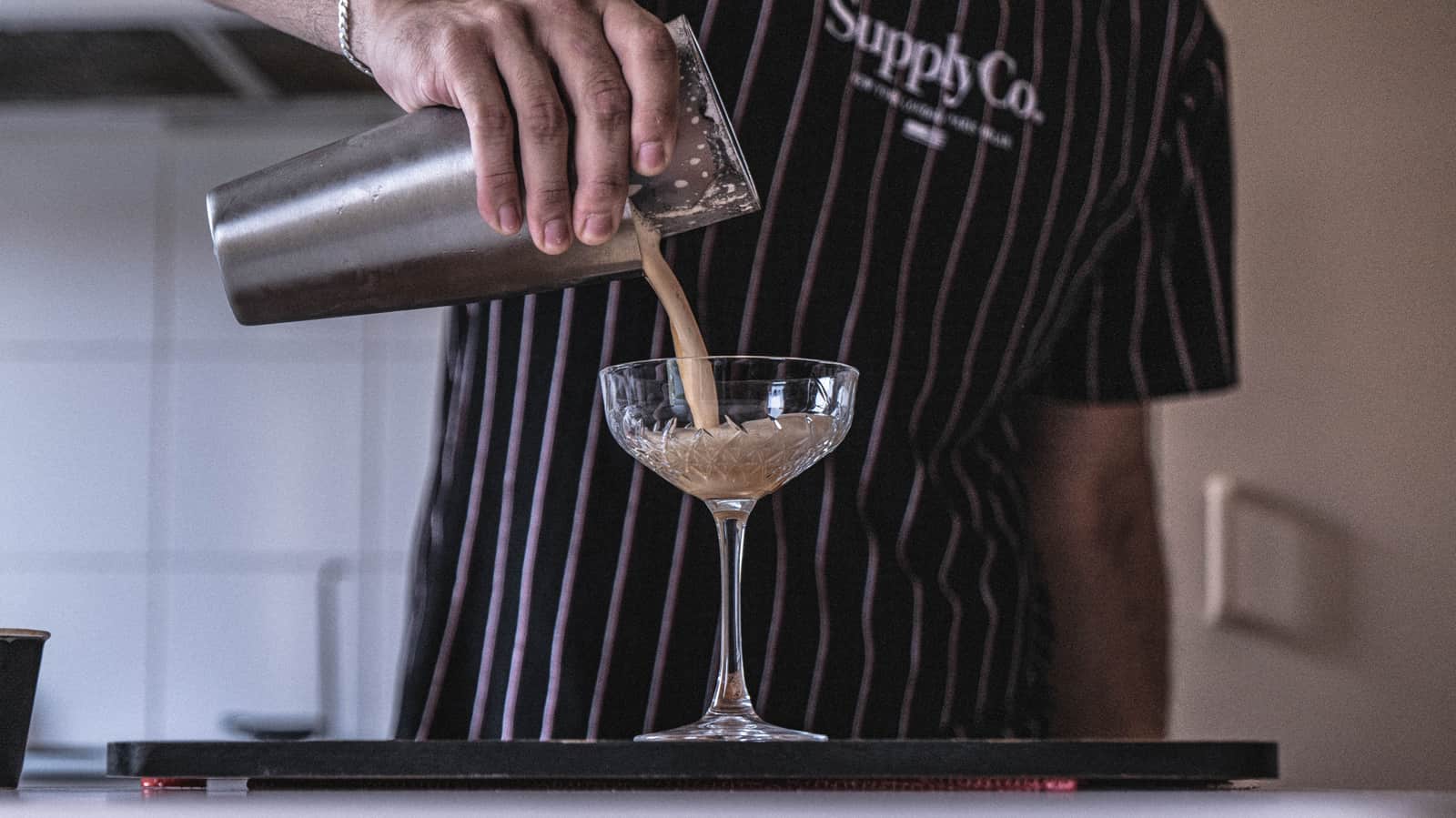 A cocktail being strained from a shaking tin into a coupe