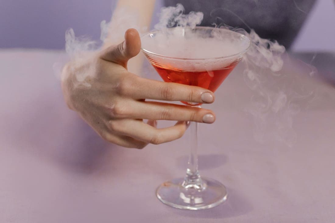 Smoke curling over a cocktail glass on a dark bar